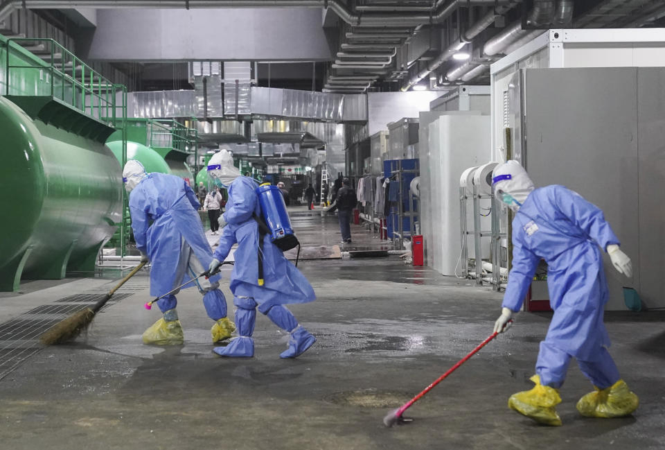 In this photo released by China's Xinhua News Agency, workers clean and disinfect the floor of a makeshift hospital at the National Exhibition and Convention Center in Shanghai, Thursday, April 14, 2022. Anti-virus controls that shut down some of China's biggest cities and fueled public irritation are spreading as infections rise, hurting a weak economy and prompting warnings of possible global shockwaves. (Ding Ting/Xinhua via AP)