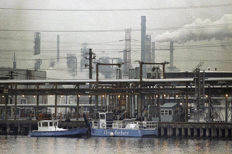 FILE —Two clean harbor cleanup boats work in the Arthur Kill waterway in front of the Exxon oil refinery in Linden, N.J., Jan. 9, 1990. A decade after Superstorm Sandy pummeled New York and New Jersey in one of the costliest storms in U.S. history, the federal government is proposing a $52 billion plan to build movable barriers and gates across bays, rivers and other waterways in the two states hardest-hit by the storm. (AP Photo/Mike Derer, File)