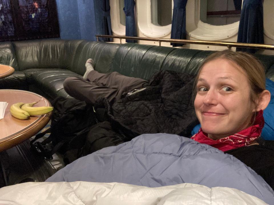 The author smiling on a couch in a sleeping bag on a ferry