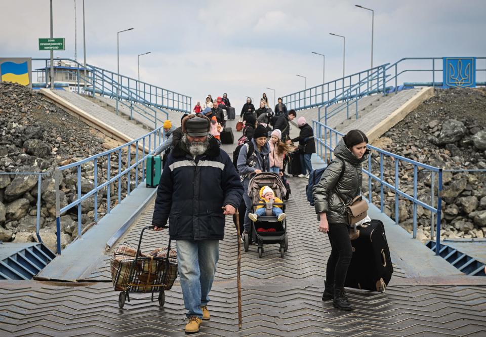 Ukrainian refugees, pulling bags and pushing strollers, embark on a ferry.