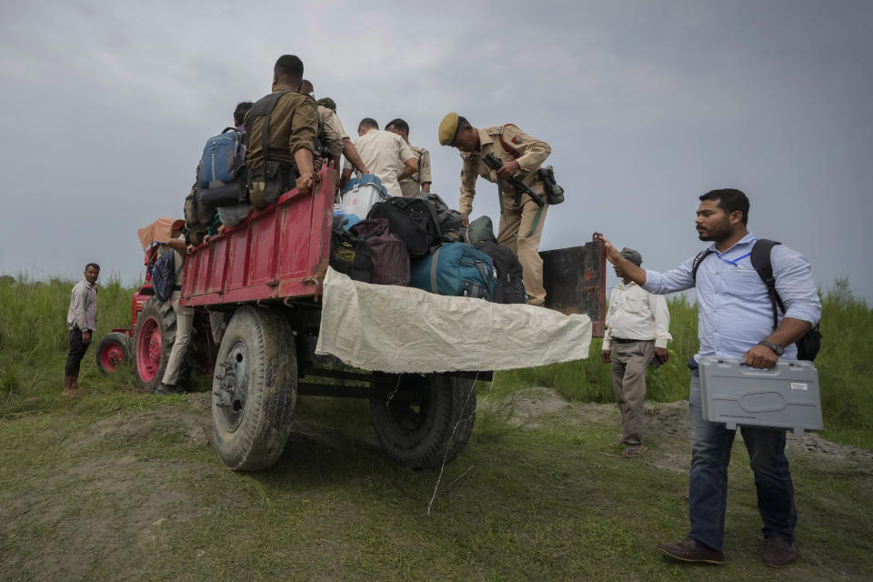 Polling officials carrying electronic voting machines and security personnel board on a tractor after disembarking from a boat after crossing the river Brahmaputra on the eve of parliament election at Baghmora Chapori (small island) of Majuli, India, April 18, 2024. (AP Photo/Anupam Nath)