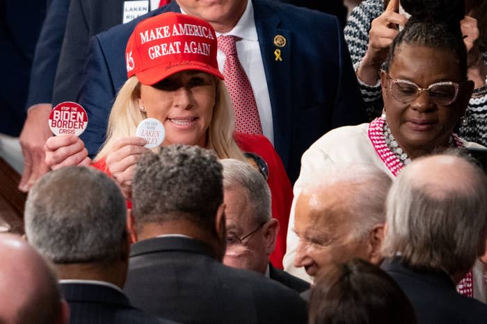 Kellyanne Conway, in a "Make America Great Again" hat, holds up buttons related to Biden's border crisis. She is surrounded by other individuals