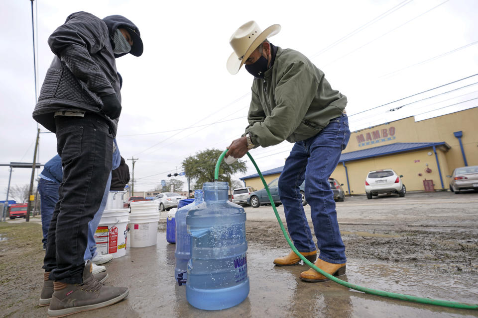 Leovardo Perez, right, fills a water jug using a hose from a public park water spigot Thursday, Feb. 18, 2021, in Houston. Texas officials have ordered 7 million people to boil tap water before drinking it following days of record low temperatures that damaged infrastructure and froze pipes.(AP Photo/David J. Phillip)