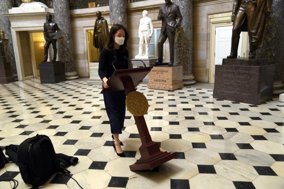 A woman tilts a lectern on a tiled floor. Statues are seen in the background.