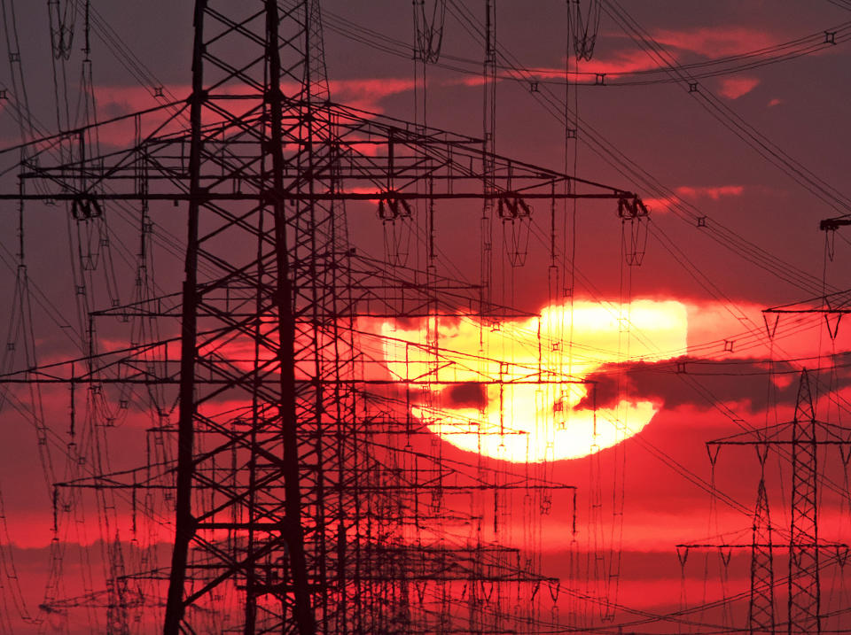 FILE-In this June 5, 2019 file photo the sun rises behind power poles near Frankfurt, Germany. Researchers calculate that the electricity required for the virtual currency bitcoin generates as much carbon dioxide as cities like Las Vegas or Hamburg. (AP Photo/Michael Probst)