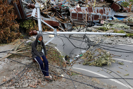 A resident sits on a fallen electric pole at Balaroa neighborhood which was hit by the earthquake and liquefaction in Palu, Central Sulawesi, Indonesia, October 11, 2018. REUTERS/Jorge Silva