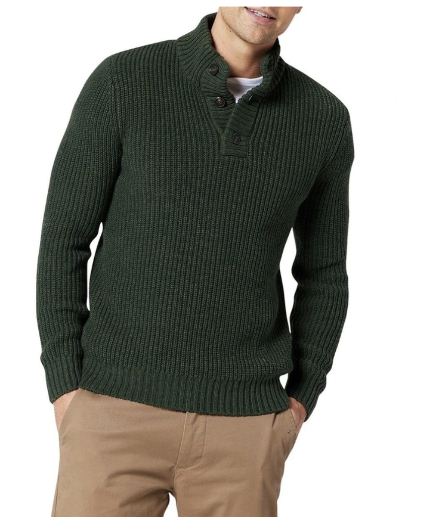 A man stands hands in chino pockets wearing olive button neck knitted jumper on a white background