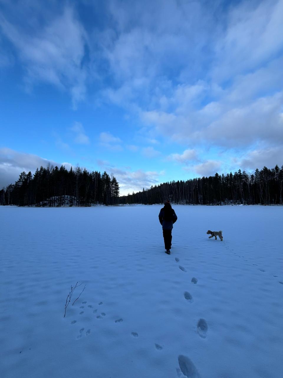 Oliver Russell walking on snow with a small dog toward an island in Finland during winter.