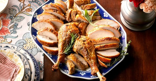 Sliced turkey breast piled on the sides of a white and blue plate with turkey legs taking up the center