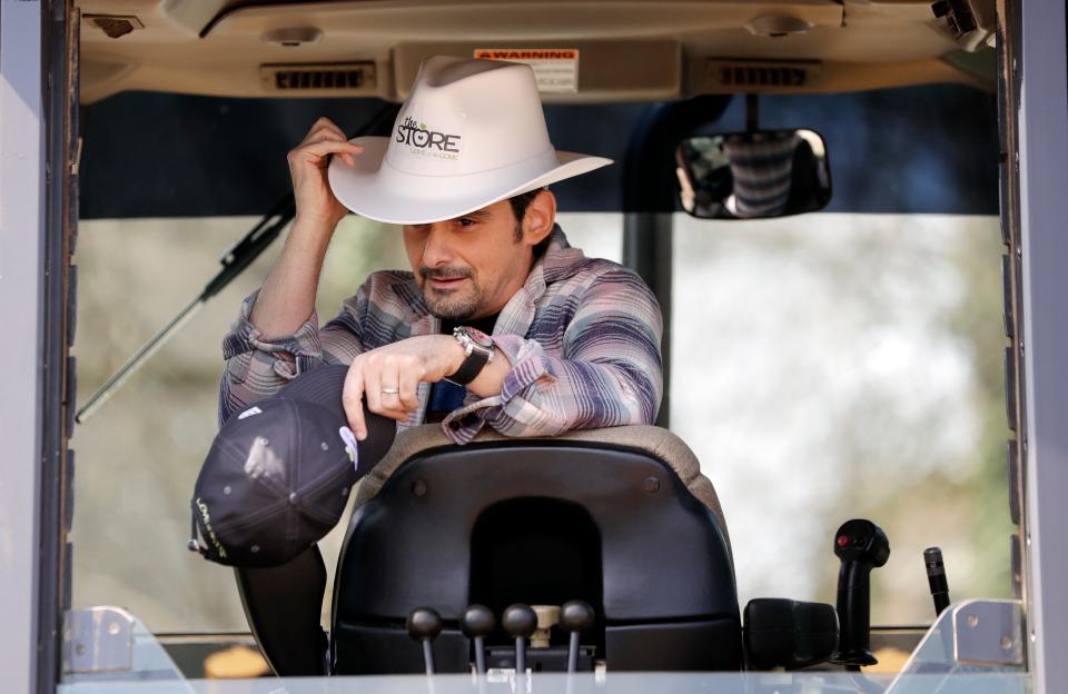 Country music star Brad Paisley puts on a hard hat shaped like a cowboy hat as he sits at the controls of a backhoe after digging a hole to break ground for The Store, a free grocery store for people in need, on April 3, 2019, in Nashville.