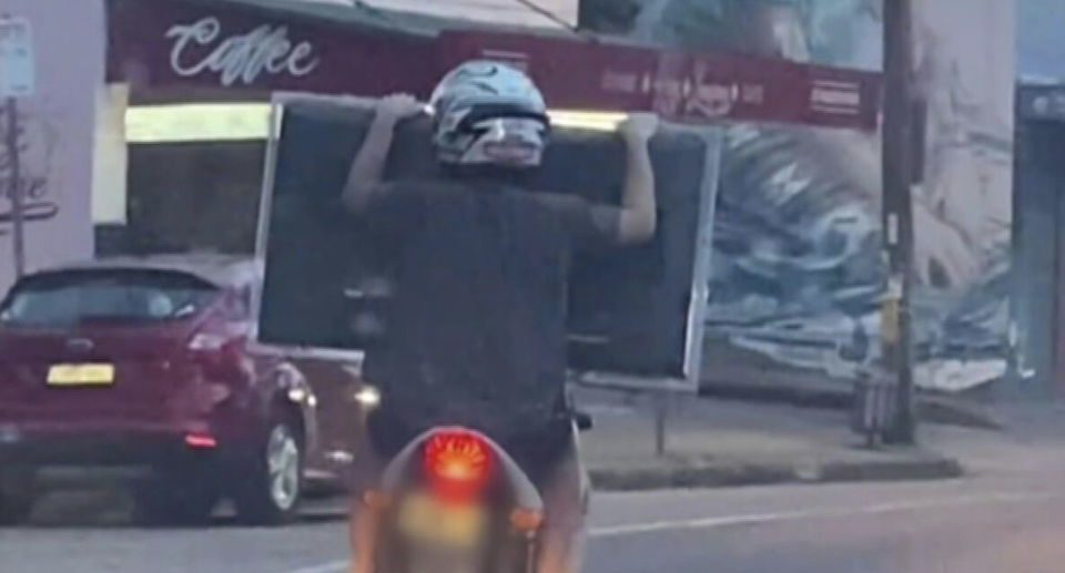 A passenger on a scooter seen holding a flatscreen TV on the road. 