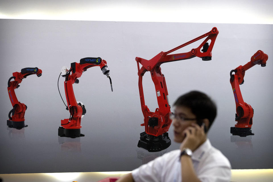 FILE - In this Aug. 15, 2018, file photo, a visitor talks on his smartphone in front of a display of manufacturing robots from a Chinese robot maker at the World Robot Conference in Beijing. In a report issued Monday, May 20, 2019, a business group says the number of foreign companies in China that feel compelled to hand over technology in exchange for market access has doubled since two years ago. (AP Photo/Mark Schiefelbein, File)