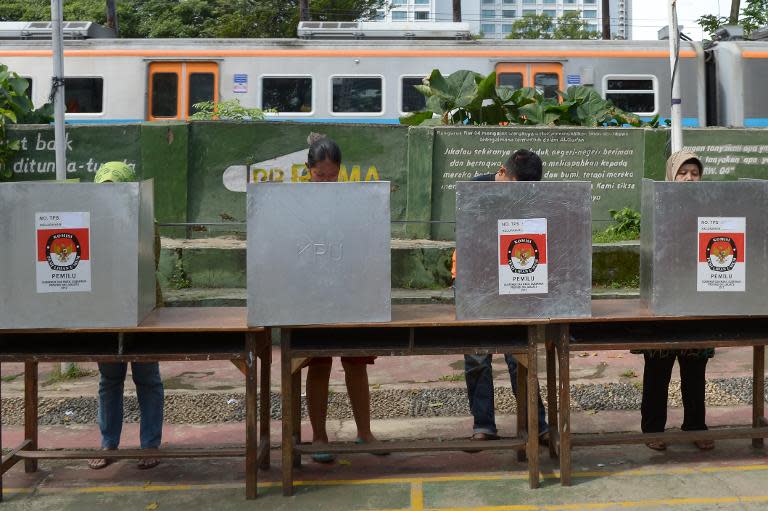 Indonesian voters cast their ballots as a train passes by at a polling station during legislative elections in Jakarta on April 9, 2014