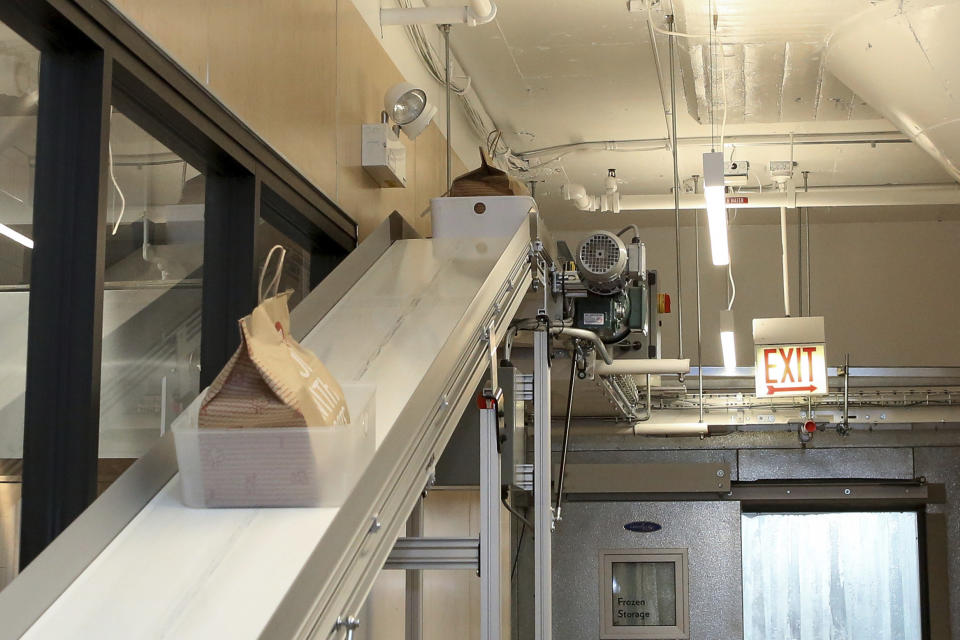 A conveyor belt takes bags of food from ghost restaurants to a room where delivery drivers pick up orders at Kitchen United's Chicago location on Aug. 29, 2019. Kitchen United, a start-up that builds kitchen commissaries for restaurants looking to enter new markets through delivery or take-out only, has plans to open 40 more kitchens in cities across the U.S. through 2020. (AP Photo/Teresa Crawford)