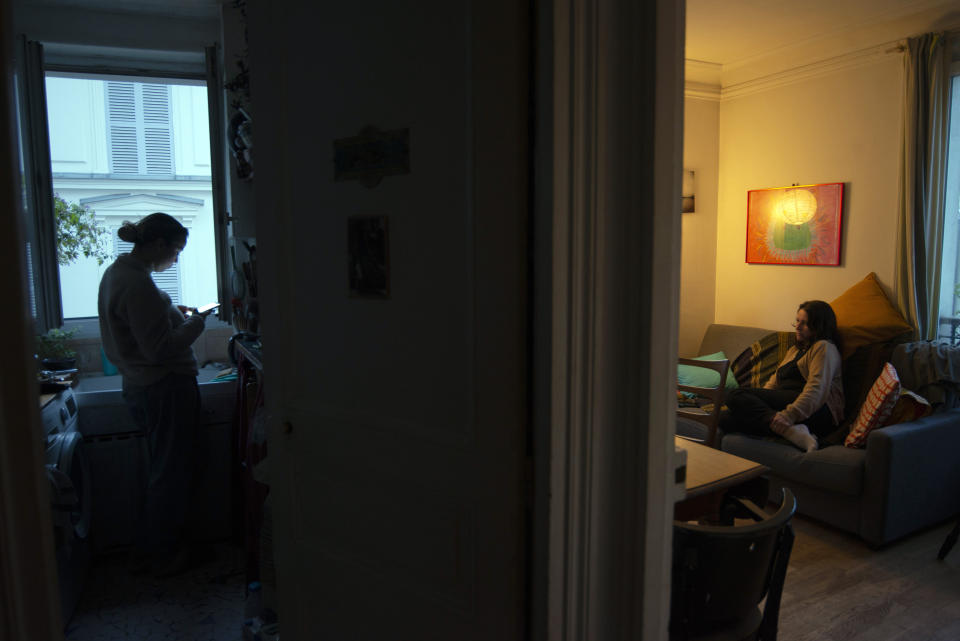 Livia Bulcao, left, consults her phone on May 22, 2021, in the kitchen of her parents' apartment in Montmartre while her mother Nathalie Sartor rests on the sofa in the sitting room. Livia, 23, moved back in her parents during the pandemic but has now found a place of her own to rent nearby in Montmartre. "I have a job. I've just found a flat. I get help from the state for housing. I can live my life as I might have done had the pandemic not happened, with inconveniences that are tiny compared to other countries. I am privileged," Livia says. (AP Photo/ Joao Luiz Bulcao)