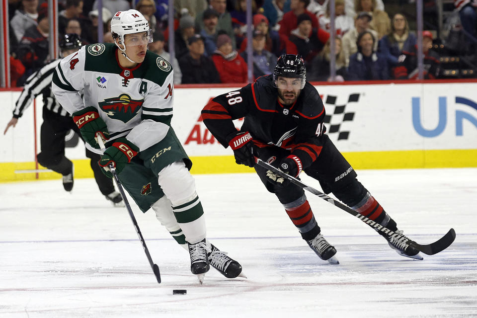 Minnesota Wild's Joel Eriksson Ek (14) moves the puck in front of Carolina Hurricanes' Jordan Martinook (48) during the first period of an NHL hockey game in Raleigh, N.C., Sunday, Jan. 21, 2024. (AP Photo/Karl B DeBlaker)