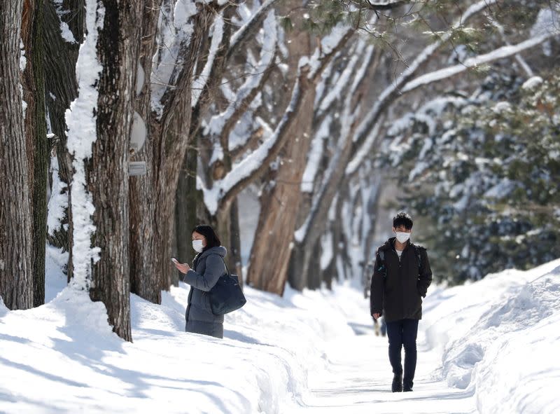 Passersby wearing protective masks walk on a snow-covered street in Sapporo, Hokkaido