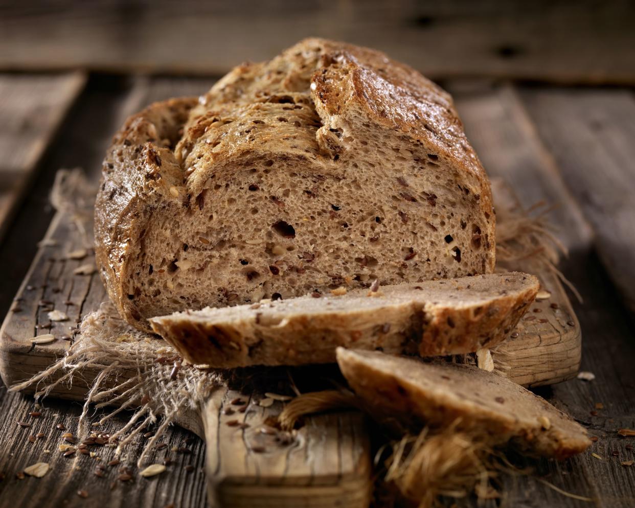 Cut artisan bread loaf with two cut slices on a rustic napkin and wooden cutting board with a blurred background of a wooden table