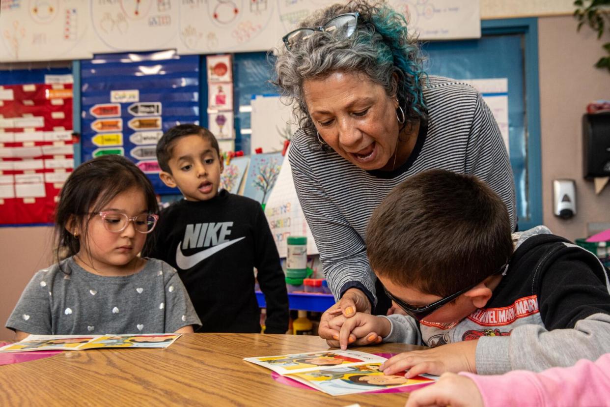 A woman helps a young boy pronounce words in a book.