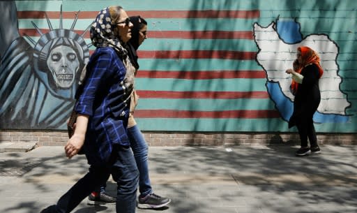 People walk by murals on the wall of the former US embassy in the Iranian capital Tehran on August 7, 2018 after US President Donald Trump warned countries against doing business with Iran