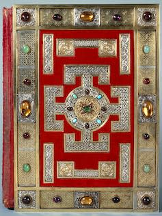 The red and bejewelled cover of a large book.