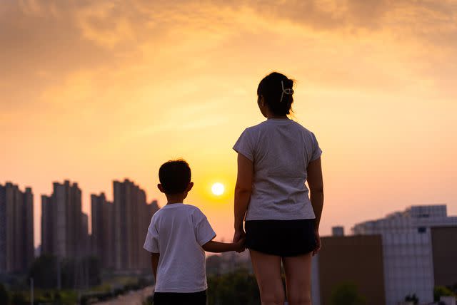 <p>Getty</p> Stock image of mom holding her child's hand looking out at a city