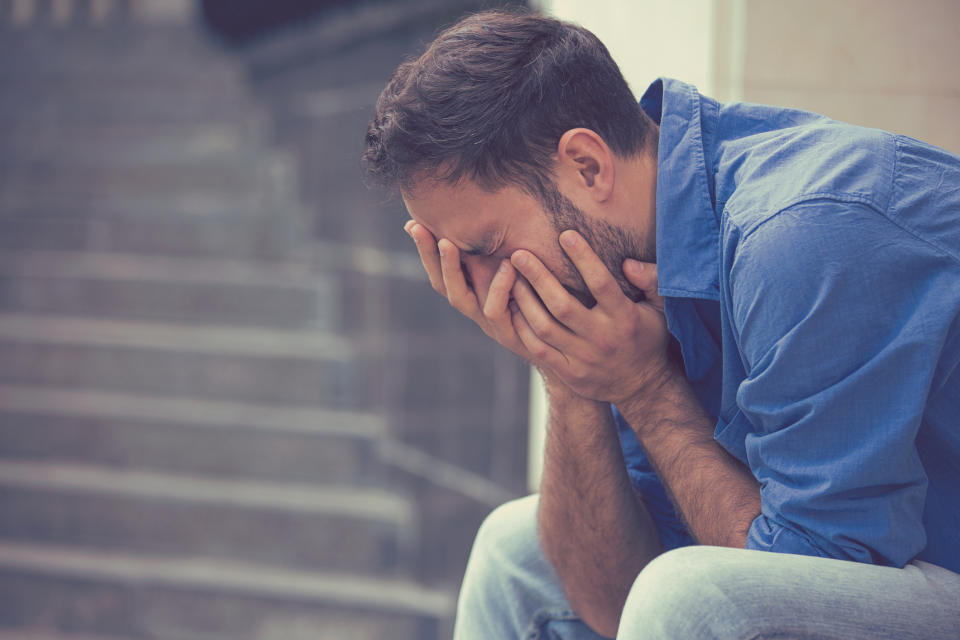 Man sitting on a step in a blue shirt crying