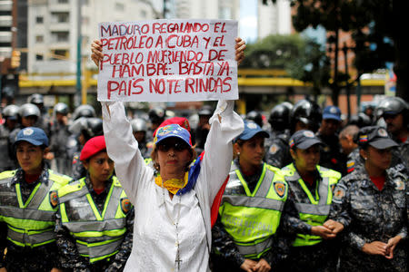 FILE PHOTO: A woman holds a sign that reads: "Maduro gives oil to Cuba and people die of hunger. Enough. Country do not give up" during a protest of workers of the health sector due to the shortages of medicines and for higher wages, outside a public children hospital in Caracas, Venezuela August 16, 2018. REUTERS/Marco Bello/File Photo