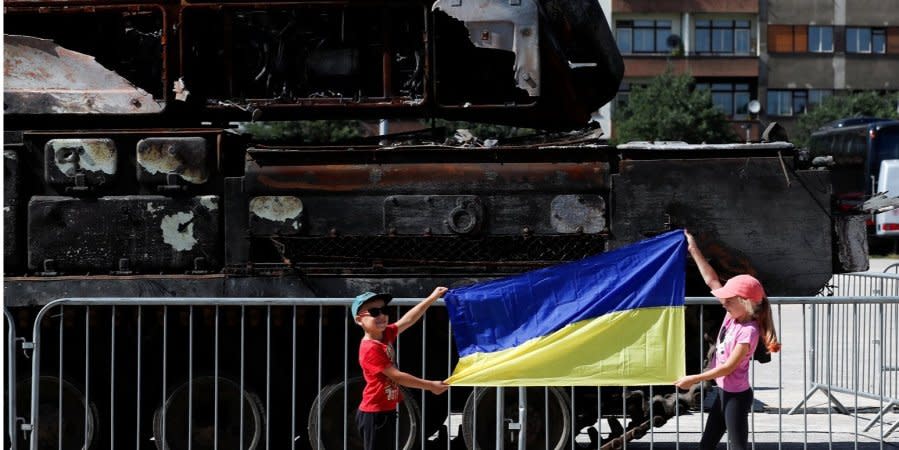 Children hold the Ukrainian flag against the background of broken Russian military equipment, which was brought from Ukraine to Prague, July 11, 2022