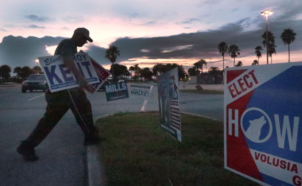 As the sun rises, a poll worker relocates campaign signs beyond the required solicitation boundary as voters started to arrive to cast ballots in the primary election on Tuesday at City Island Library in Daytona Beach.