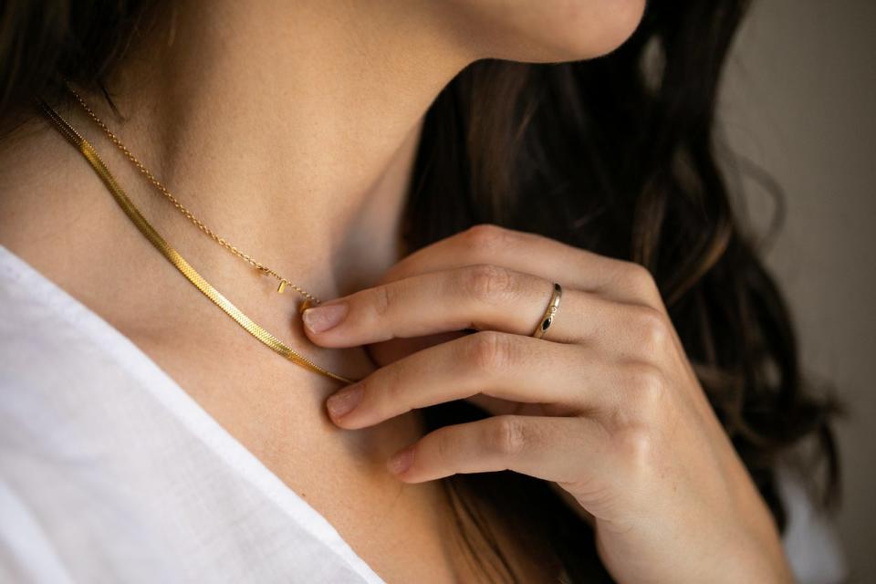 Closeup of neck of brunette woman in white t-shirt wearing a gold necklace and a ring on one hand