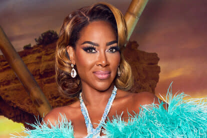 Kenya Moore in a teal feathered and crystal embellished fitted gown in front of a Portugal inspired set.