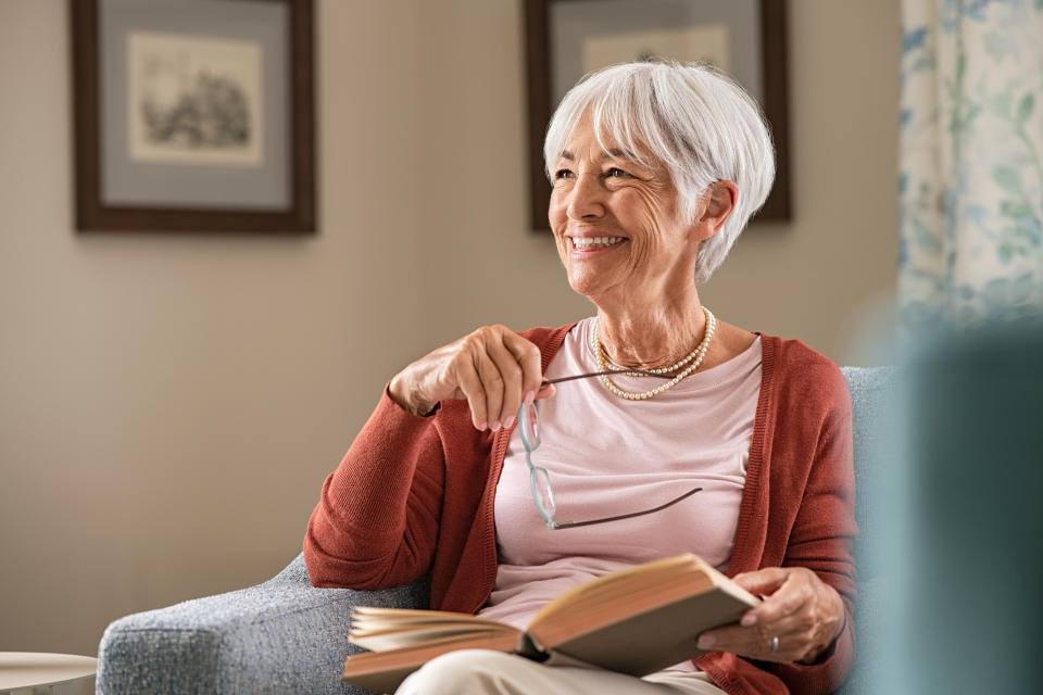 An older woman with short gray hair holds her glasses while reading a book while seated.