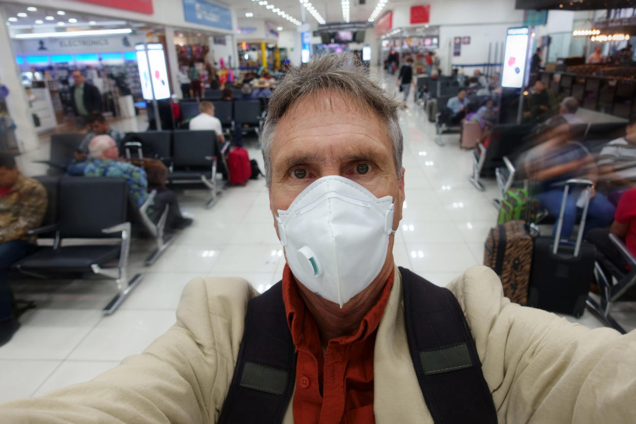 Man taking a selfie while wearing protective face mask in airport. 