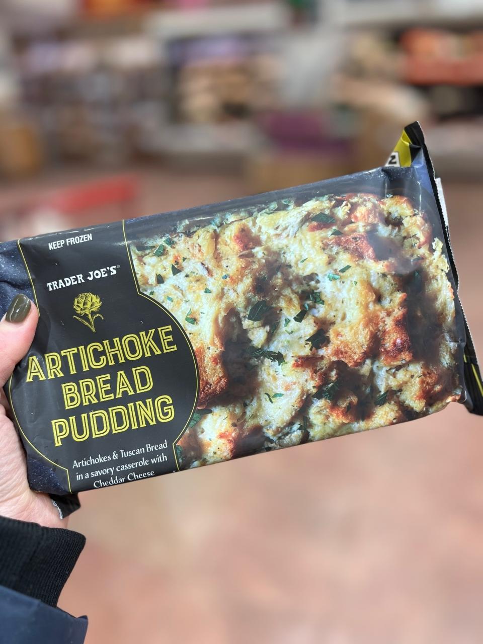 Hand holding Trader Joe's Artichoke Bread Pudding package in a store