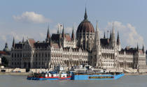 FILE - In this Tuesday, June 11, 2019, file photo, a barge carries the sightseeing boat, right, past the house of parliament on the Danube river after it was lifted from riverbed in Budapest, Hungary. Preparations are underway for commemorations to be held on the first anniversary of the May 29, 2019, mishap on the Danube River in which a sightseeing boat carrying mostly tourists from South Korea sank after a collision with a river cruise ship. Just seven of the 33 South Korean tourists aboard the Hableany (Mermaid) survived the nighttime collision. (AP Photo/Darko Bandic, File)