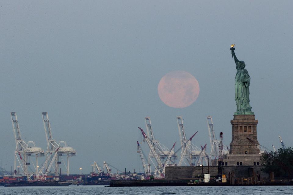 FILE - In this June 23, 2013 file photo, a supermoon sets near the Statue of Liberty in New York. The Statue of Liberty, which has been closed to visitors since Superstorm Sandy, is scheduled to reopen for tours July Fourth, when Statue Cruises resumes departures for Liberty Island from Lower Manhattan. But for tourists who want a photo of the famous statue without visiting the island, there are many options, including a variety of vantage points around the Lower Manhattan waterfront. (AP Photo/Julio Cortez, file)