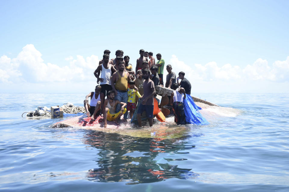 Refugiados rohinya esperan sobre el casco de la embarcación naufragada en la que viajaban a ser rescatados, en aguas de Aceh Occidental, Indonesia, el 21 de marzo de 2024. (AP Foto/Reza Saifullah)