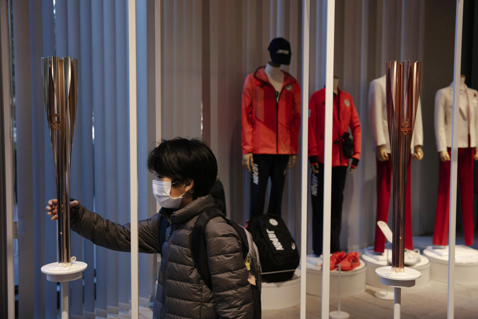 A boy with a mask poses with an Olympic torch of the Tokyo 2020 Olympics while visiting Tokyo Olympic Museum, Sunday, Feb. 23, 2020, in Tokyo. (AP Photo/Jae C. Hong)