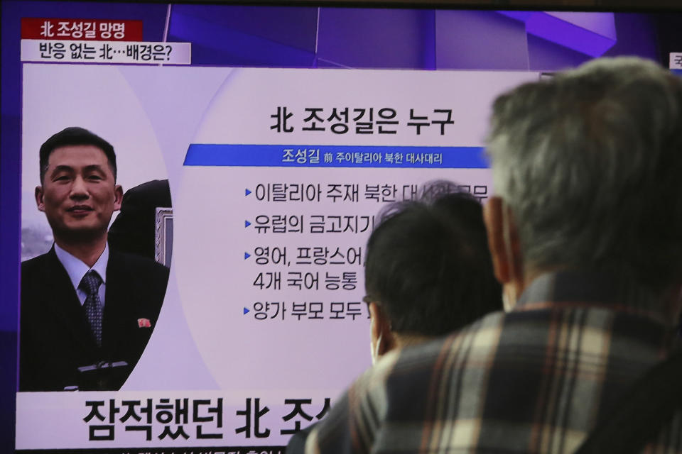 People watch a TV showing an image of Jo Song Gil, the North Korea's former ambassador to Italy, during a news program at the Seoul Railway Station in Seoul, South Korea, Wednesday, Oct. 7, 2020. Jo who had vanished in Italy in late 2018, lives in South Korea under government protection, a lawmaker said Wednesday. The Korean letters read: "Who is the North Korean Jo Song Gil." (AP Photo/Ahn Young-joon)