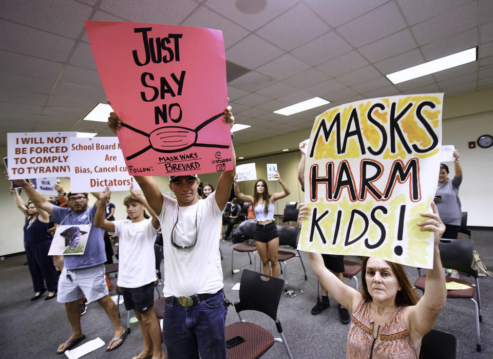 People demonstrate inside a school with placards reading: I will not be forced to comply with tyranny, Just say no, and Masks harm kids.