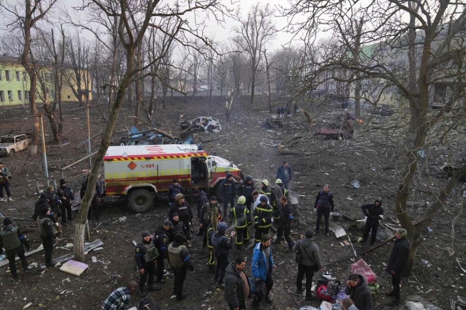 Ukrainian servicemen and firefighters stand in the area outside of a maternity hospital damaged in a shelling attack in Mariupol (AP)