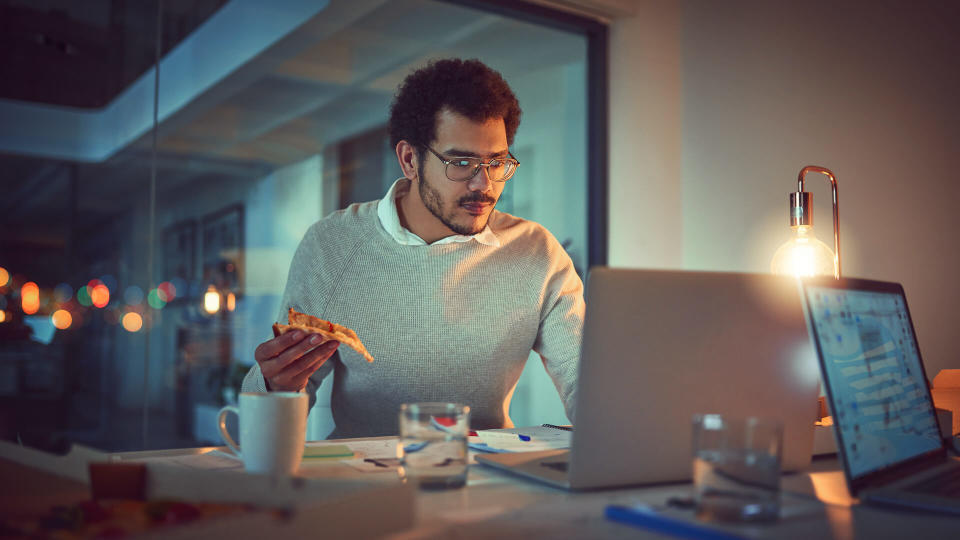 Shot of a young designer eating pizza while working late in an office.