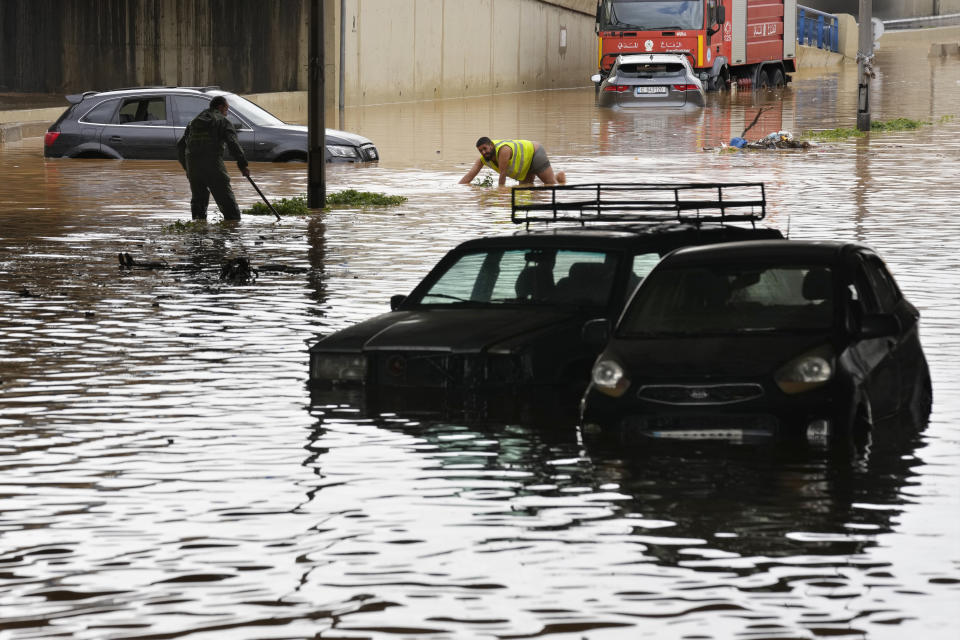 Workers try to open the sewers between submerged cars at a highway flooded by the rains, in Beirut, Lebanon, Saturday, Dec. 23, 2023. A rainstorm has paralysed parts of Lebanon's cities, turning streets to small rivers, stranding motorists inside their vehicles and damaging homes in some areas. (AP Photo/Hussein Malla)