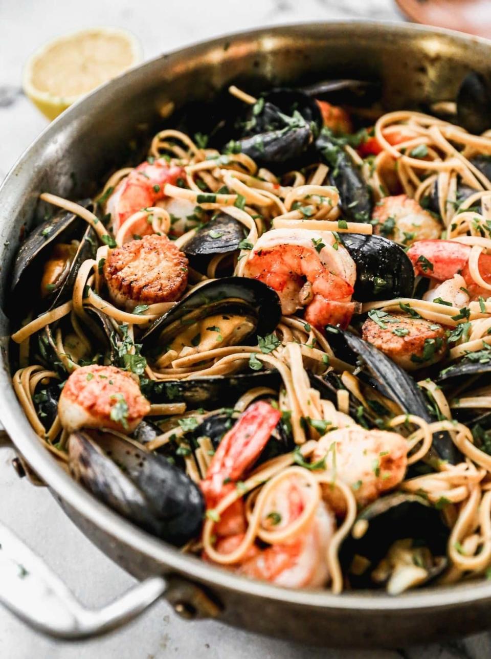 A skillet filled with seafood pasta, including shrimp and mussels, garnished with slices of lemon