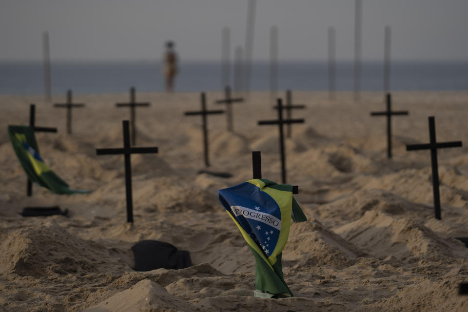 A Brazilian flag hangs on a cross marking a symbolic grave dug by activists from the NGO Rio de Paz to protest the government's handling of the COVID-19 pandemic, on Copacabana beach in Rio de Janeiro, Brazil, Thursday, June 11, 2020. A Brazilian Supreme Court justice ordered the government of President Jair Bolsonaro to resume publication of full COVID-19 data, including the cumulative death toll, following allegations the government was trying to hide the severity of the pandemic in Latin America’s biggest country. (AP Photo/Leo Correa)