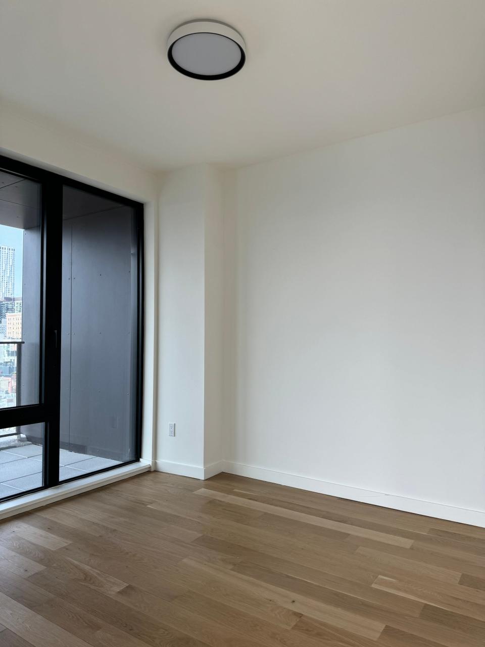 An empty bedroom with floor-to-ceiling windows on one wall.