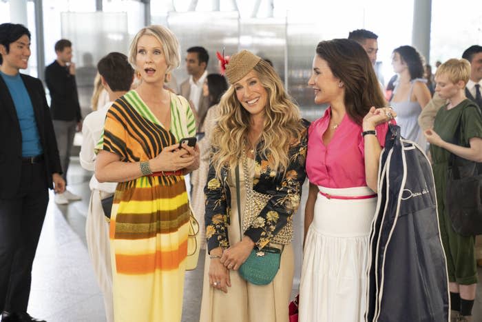 Carrie, Miranda and Charlotte stand in a lobby smiling