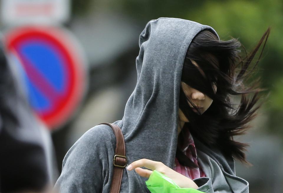 A woman's hair blows across her face as she struggles to walk in a strong wind caused by an approaching tropical storm Man-yi in Tokyo