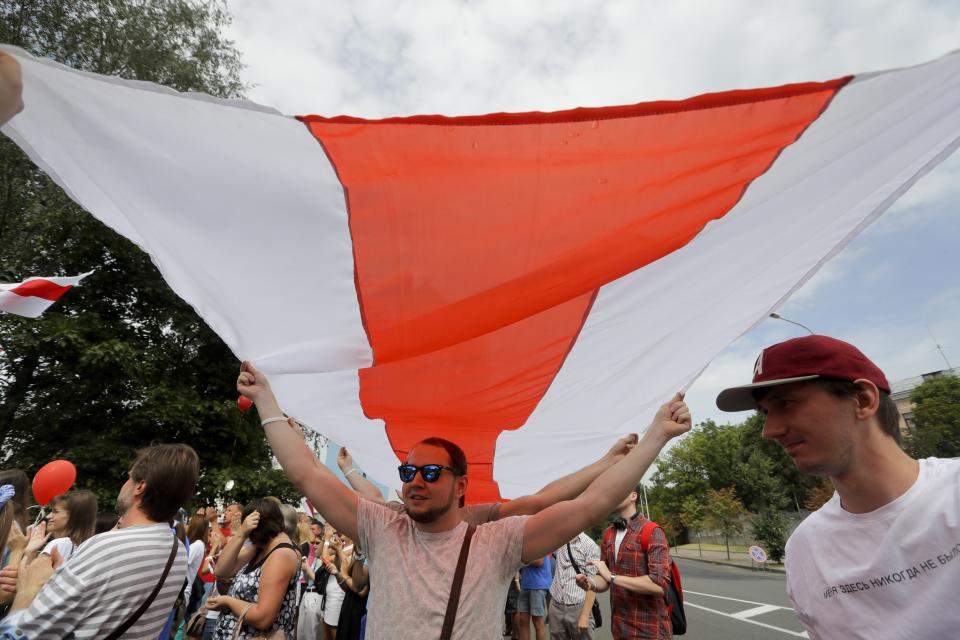 People with an old Belarusian flag gather to show their solidarity with the detainees at a detention center during opposition rally in Minsk, Belarus, Tuesday, Aug. 18, 2020. After the police crackdown at least 7,000 were detained by riot police, with many complaining they were beaten mercilessly. (AP Photo/Sergei Grits)